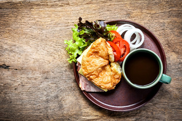 Coffee and ham cheese croissant sandwich as breakfast beside the garden.Flat lay shot.