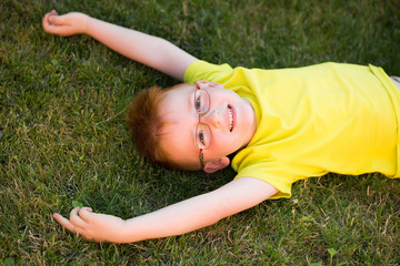 Fototapeta premium Happy baby boy with red hair in glasses on grass