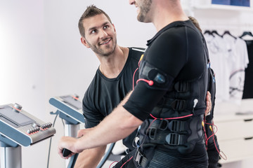 Trainer helping man in EMS gym to exercise correctly