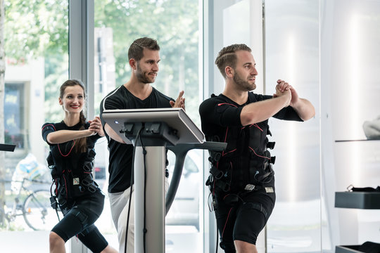 Woman and man doing chest exercises in EMS gym, studio, a trainer is helping them