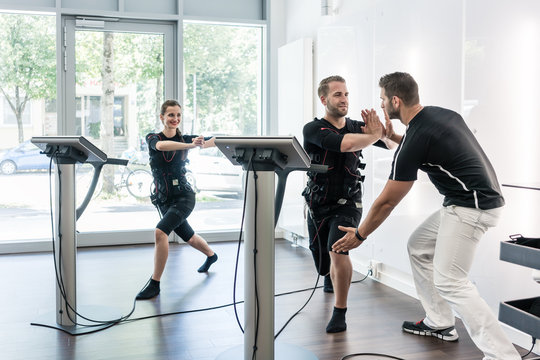 Woman and man doing chest exercises in EMS gym, studio, a trainer is helping them