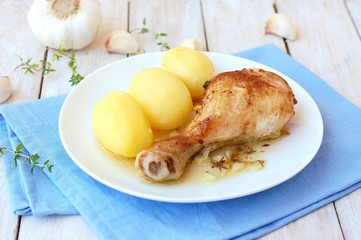Roasted chicken with fresh garlic, thyme and potatoes on white plate on blue cloth on wooden background