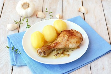 Roasted chicken with fresh garlic, thyme and potatoes on white plate on blue cloth on wooden background