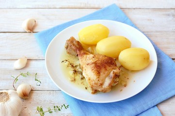 Roasted chicken with fresh garlic, thyme and potatoes on white plate on blue cloth on wooden background