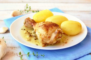 Roasted chicken with fresh garlic, thyme and potatoes on white plate on blue cloth on wooden background