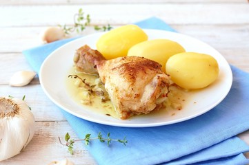 Roasted chicken with fresh garlic, thyme and potatoes on white plate on blue cloth on wooden background