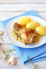 Roasted chicken with fresh garlic, thyme and potatoes on white plate on blue cloth on wooden background