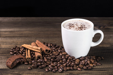 cup of coffee with coffee beans, cookie and cinnamon on wooden table. Image with copy space