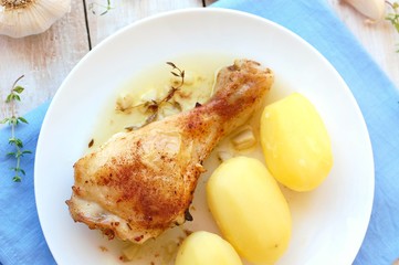 Roasted chicken with fresh garlic, thyme and potatoes on white plate on blue cloth on wooden...