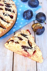 Piece of summer cake with plums on blue cloth on wooden background