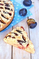Piece of summer cake with plums on blue cloth on wooden background