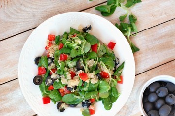 Fresh healthy vegan salad with quinoa, corn salad, black olives, red pepper and olive oil on white plate cloth on white wooden background