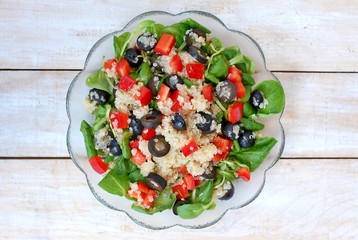 Fresh healthy vegan salad with quinoa, corn salad, black olives, red pepper and olive oil in glass bowl cloth on white wooden background