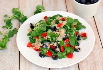 Fresh healthy vegan salad with quinoa, corn salad, black olives, red pepper and olive oil on white plate cloth on white wooden background
