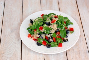 Fresh healthy vegan salad with quinoa, corn salad, black olives, red pepper and olive oil on white plate cloth on white wooden background