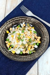 Healthy vegan meal with rice, chickpeas, sweet corn, peas, green beans and rice on dark plate on jeans cloth on wooden background