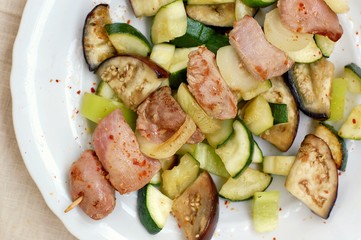 Skewer with roasted turkey hen meat with onion, zucchini and aubergine on white plate