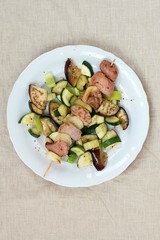 Skewer with roasted turkey hen meat with onion, zucchini and aubergine on white plate