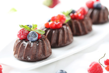 Sweet chocolate cakes with berries on white wooden table