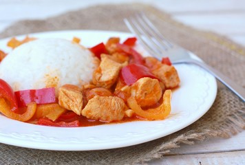 Meal from chicken meat with Indian spices, green and red pepper and rice on white plate, gunny cloth and wood with fork