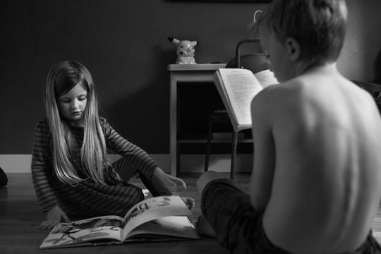 Two children sitting together indoors, looking at book, black and white