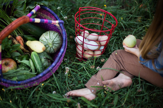 Young girl sitting in garden with vegetables and eggs
