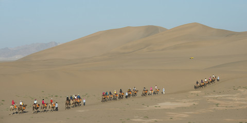Fototapeta na wymiar Tourists riding camels at Mingsha Shan, Dunhuang, Jiuquan, Gansu