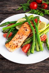 Fried salmon with asparagus, tomatoes, lemon, yellow lime on white plate