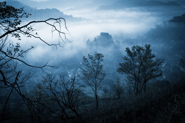Mysterious misty morning over Biertan village, Transylvania, Romania. Blue colors. spooky,...