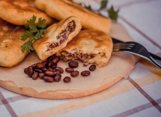 Fried tasty patties filled boiled beans and fried onion, on wooden plate, checked tablecloth on the background. Delicious buns on a baking sheet.