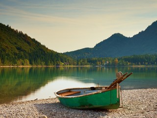 Abandoned fishing paddle boat on bank of Alps lake. Morning lake glowing by sunlight.
