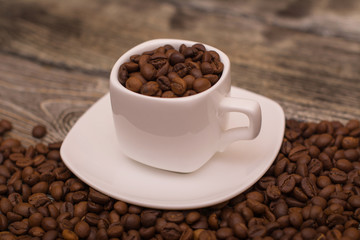 small white cup with coffee beans on wooden background
