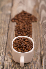small white cup with coffee beans in the shape of an arrow on wooden background