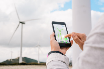 Engineer woman managing energy production app touching phone screen at wind turbine farm park...