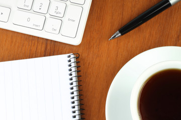 Keyboard, coffee, notepad and pen on wooden background .