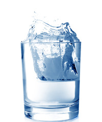 Ice in glass of water with splash on white background .