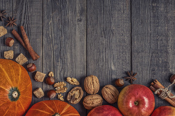 Wooden background with pumpkin, apples, nuts and spices.