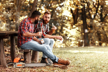 Two friends Lumberjack worker sitting in the forest eating burgers and drinking beer.Resting after...