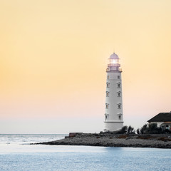 Lighthouse searchlight beam near ocean at sunset