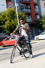 Young handsome guy with a bicycle on street looking at mobile phone.