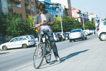 Young handsome guy with a bicycle on street looking at mobile phone.
