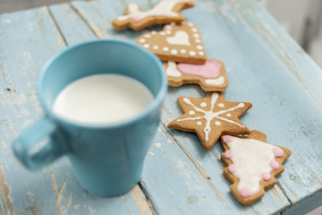 Obraz na płótnie Canvas Ginger bread winter cookies with handmade icing on a blue table with a cup of milk