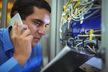 Technician talking on mobile phone while analyzing server