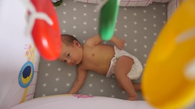 Newborn in a diaper. Top view through a colorful mobile toy elements