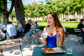 Beautiful woman in the blue dress sitting at the cafe with coffee and croissant outdoors at the park.
