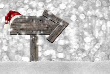 Christmas wooden sign with a Santa Hat hanging on it in a snowy