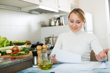 Cheerful housewife signing papers in kitchen