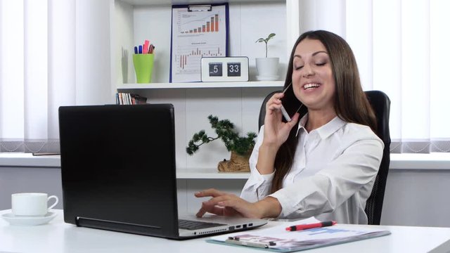 Business woman sitting in the office in front of a laptop and talking on the phone
