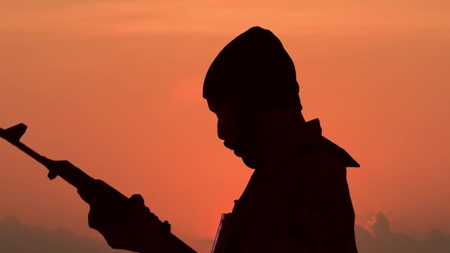 Silhouette of man shooting in air with rifle at dawn