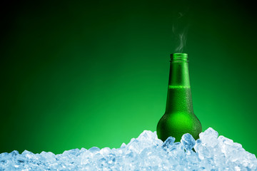 Bottle of cold beer in ice on green background